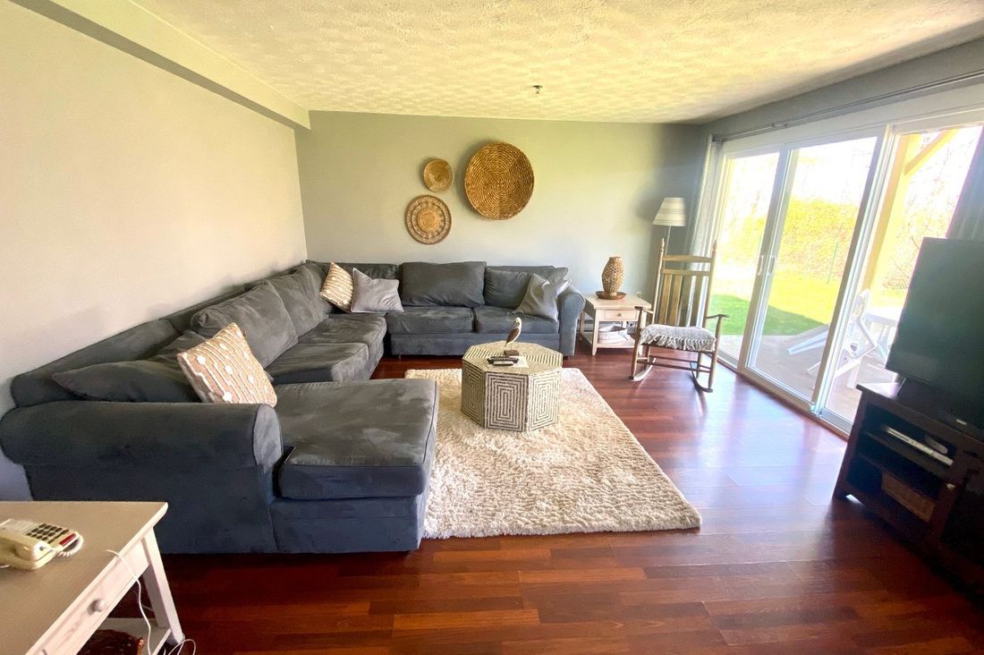 The living room of a two-bedroom condominium suite at Village by the Sea, with a sectional sofa, hardwood floors and a slider onto the private deck