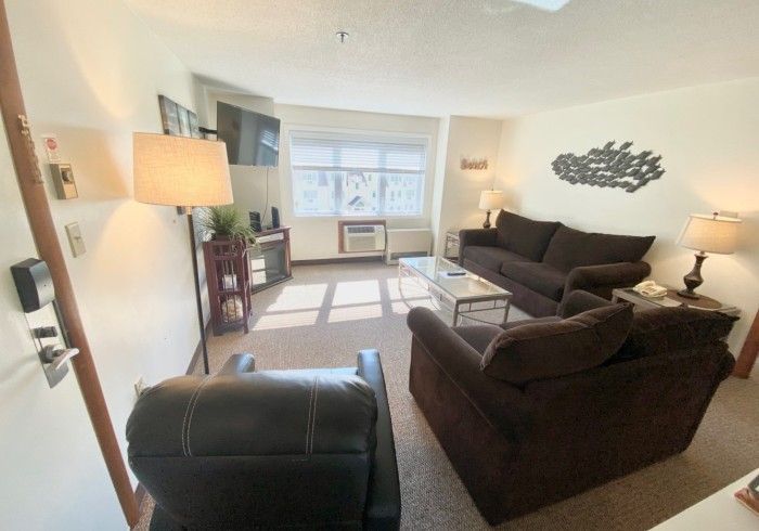 A comfort one-bedroom suite living room with brown furniture and a bright window at Village by the Sea, Wells, Maine