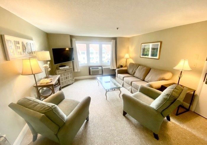 A premium one-bedroom suite living room with two armchairs, a sofa and a large window at Village by the Sea, Wells, Maine